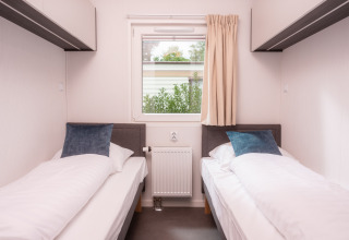 Zwei Einzelbetten und ein Fenster in einem hellen Zimmer der Tiny Cabin im Holiday Park Mölke, Niederlande.