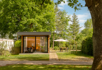 Tiny Cabin at Holiday Park Mölke in the Netherlands, set among green trees with an outdoor seating area and umbrella.
