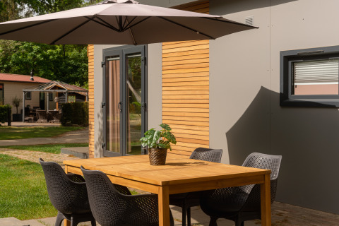 Buiten eettafel met stoelen en parasol bij Tiny Cabin in Holiday Park Mölke, Nederland, in de zomer.