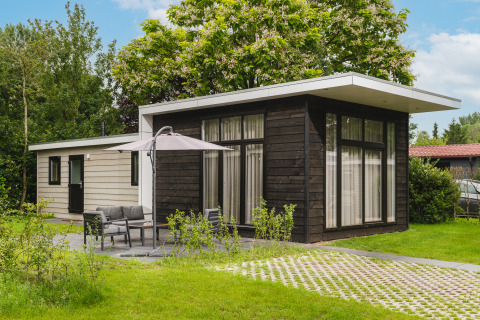 Exterior de Cosy Cabin, una cabaña moderna rodeada de césped, árboles y muebles de jardín.