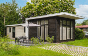 Exterior of Cosy Cabin, a modern cabin surrounded by green lawn, trees, patio and outdoor furniture.
