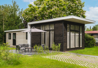 Buitenzijde van Cosy Cabin, een moderne hut met terras, tuinmeubilair, gras en omringende bomen.