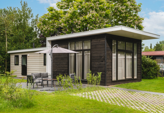 Exterior de Cosy Cabin, una cabaña moderna rodeada de césped, árboles y muebles de jardín.