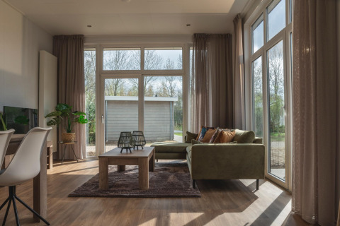 Helles Wohnzimmer im Cosy Cabin im Holiday Park Mölke, Niederlande, mit großen Fenstern und grünem Sofa.
