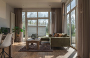 Bright living room at Cosy Cabin in Holiday Park Mölke, Netherlands, with large windows and a green sofa.