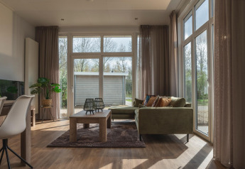Helles Wohnzimmer im Cosy Cabin im Holiday Park Mölke, Niederlande, mit großen Fenstern und grünem Sofa.