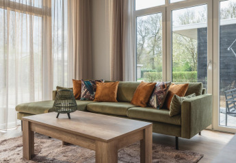 Hyggelig stue i Cosy Cabin ved Holiday Park Mölke, Holland, med grøn sofa, træbord og store vinduer.