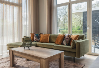 Gezellige woonkamer in Cosy Cabin bij Holiday Park Mölke, Nederland, met groene bank en houten tafel.