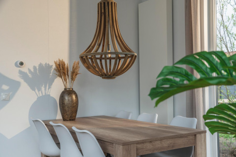 Dining area at Cosy Cabin in Holiday Park Mölke featuring wood table, white chairs, and wooden light fixture.