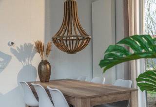 Eethoek in Cosy Cabin bij Holiday Park Mölke met houten tafel, witte stoelen en houten hanglamp.