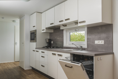 Cocina moderna de glamping con armarios blancos, lavavajillas abierto y cafetera sobre la encimera.