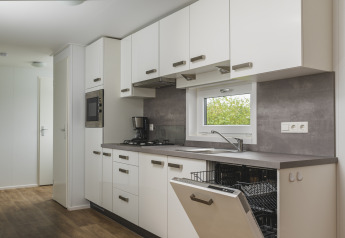 Cocina moderna de glamping con armarios blancos, lavavajillas abierto y cafetera sobre la encimera.