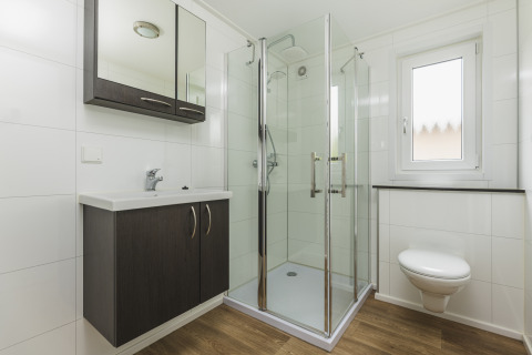 Baño moderno con ducha acristalada, inodoro suspendido y lavabo sobre suelo con acabado madera en glamping.