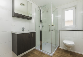 Moderne badkamer met glazen douche, hangtoilet, wastafel en houtlook vloer in glamping accommodatie.