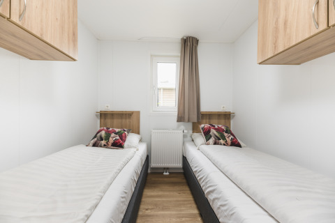 Dos camas individuales en un alojamiento glamping, con paredes blancas, armarios de madera y cojines coloridos.
