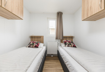 Dos camas individuales en un alojamiento glamping, con paredes blancas, armarios de madera y cojines coloridos.