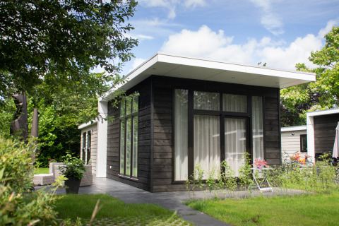 Modernes, schwarzes Holzhaus mit großen Fenstern im Grünen im Holiday Park Mölke in den Niederlanden.