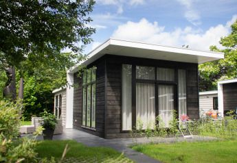 Moderne zwarte houten chalet met grote ramen bij Holiday Park Mölke in Nederland, omgeven door groen.