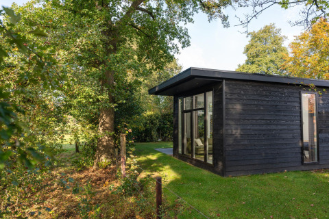 Naturhytte ved Holiday Park Mölke i Holland, omgivet af grønne træer og en frodig græsplæne.