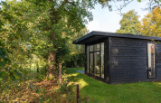 Naturhütte im Holiday Park Mölke in den Niederlanden, umgeben von Bäumen und grünem Rasen.