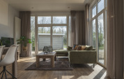 Lys stue i Cosy Cabin ved Holiday Park Mölke i Holland med store vinduer, grøn sofa og træbord.