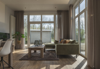 Lys stue i Cosy Cabin ved Holiday Park Mölke i Holland med store vinduer, grøn sofa og træbord.