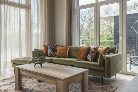 Moderne living met groene zetel en houten tafel in Cosy Cabin, Holiday Park Mölke, Nederland.