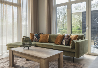 Moderne living met groene zetel en houten tafel in Cosy Cabin, Holiday Park Mölke, Nederland.