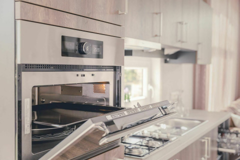 Horno empotrado moderno con puerta abierta en una cocina luminosa y acogedora de Cosy Cabin en Holiday Park Mölke.