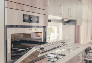 Horno empotrado moderno con puerta abierta en una cocina luminosa y acogedora de Cosy Cabin en Holiday Park Mölke.