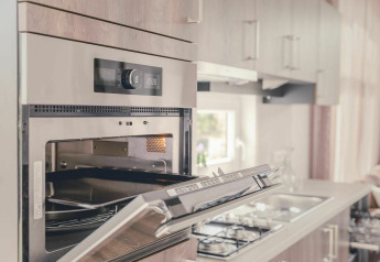 Horno empotrado moderno con puerta abierta en una cocina luminosa y acogedora de Cosy Cabin en Holiday Park Mölke.