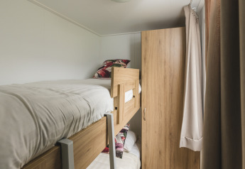 Stanza glamping compatta con letti a castello in legno, lenzuola bianche, armadio e tende beige.