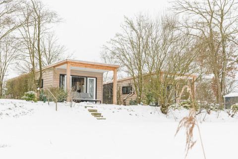 River Lodge at Holiday Park Mölke in the Netherlands, surrounded by snow, trees, and a wintry landscape.