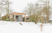 River Lodge at Holiday Park Mölke in the Netherlands, surrounded by snow, trees, and a wintry landscape.