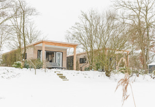 River Lodge im Holiday Park Mölke, Niederlande, umgeben von verschneiter Winterlandschaft und Bäumen.