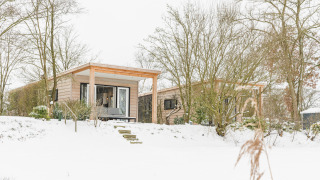 River Lodge au Holiday Park Mölke aux Pays-Bas, entouré de neige, d'arbres et d’un paysage hivernal.