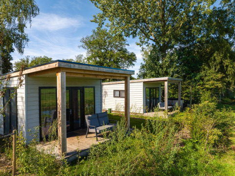 Twee River Lodge-huisjes in Holiday Park Mölke, Nederland, omringd door groen en bomen.
