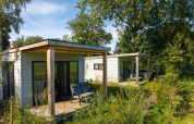To moderne River lodge-hytter på Holiday Park Mölke i Holland, omgivet af grønne træer og planter.