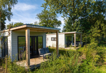 Twee River Lodge-huisjes in Holiday Park Mölke, Nederland, omringd door groen en bomen.