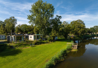 River Lodge al Holiday Park Mölke nei Paesi Bassi, accanto al fiume e circondato da prato e alberi verdi.