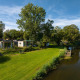 Chalets River Lodge au Holiday Park Mölke, Pays-Bas, en bord de rivière avec pelouse et arbres verts.