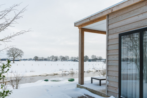 Vista invernal desde River Lodge en Holiday Park Mölke en los Países Bajos, con nieve y río tranquilo.