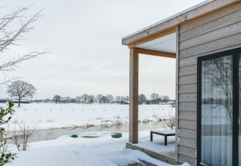Vista invernal desde River Lodge en Holiday Park Mölke en los Países Bajos, con nieve y río tranquilo.