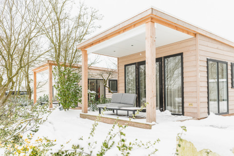 River Lodge im Holiday Park Mölke in den Niederlanden, umgeben von Schnee, mit gemütlicher Terrasse.