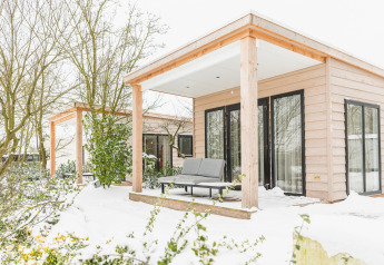 River Lodge ved Holiday Park Mölke i Nederlandene, omgivet af sne og træer, med udendørs siddeområde.
