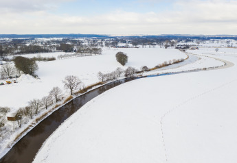 Luchtzicht op River Lodge bij Vakantiepark Mölke in Nederland, met een rivier en besneeuwde weiden.