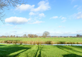 Grønt landskab med træer, flod og blå himmel ved River Lodge i Holiday Park Mölke, Holland.