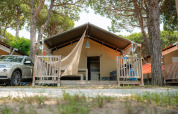 Safari tent Villatent Outback with porch, car parked beside, surrounded by trees on a sunny day.