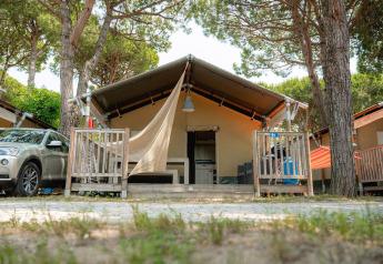 Safari tent Villatent Outback with porch, car parked beside, surrounded by trees on a sunny day.