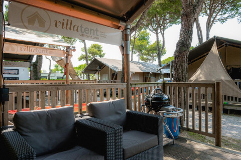 Terraza exterior en Villatent Outback con sillones de mimbre, barbacoa y tiendas safari de lujo alrededor.